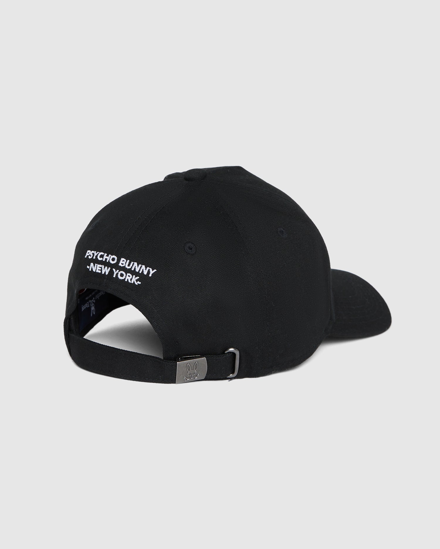 Back view of the men's Kingwood embroidered baseball cap (B6A916Y1HT) by Psycho Bunny in black, featuring white embroidered text that reads "PSYCHO BUNNY NEW YORK" above the adjustable backstrap. The cap has a metal buckle on the strap for size adjustment. Plain grey background.