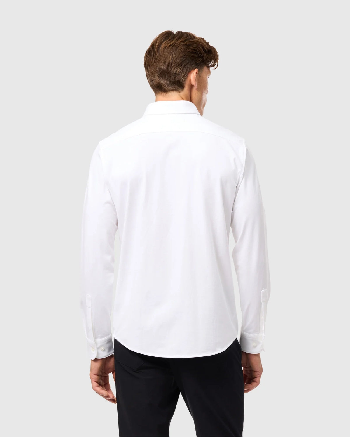 A man with brown hair is facing away, wearing a Psycho Bunny MENS ARTHUR JERSEY SHIRT - B6C748D200 crafted from stretch Pima cotton, paired with black pants against a light gray background.