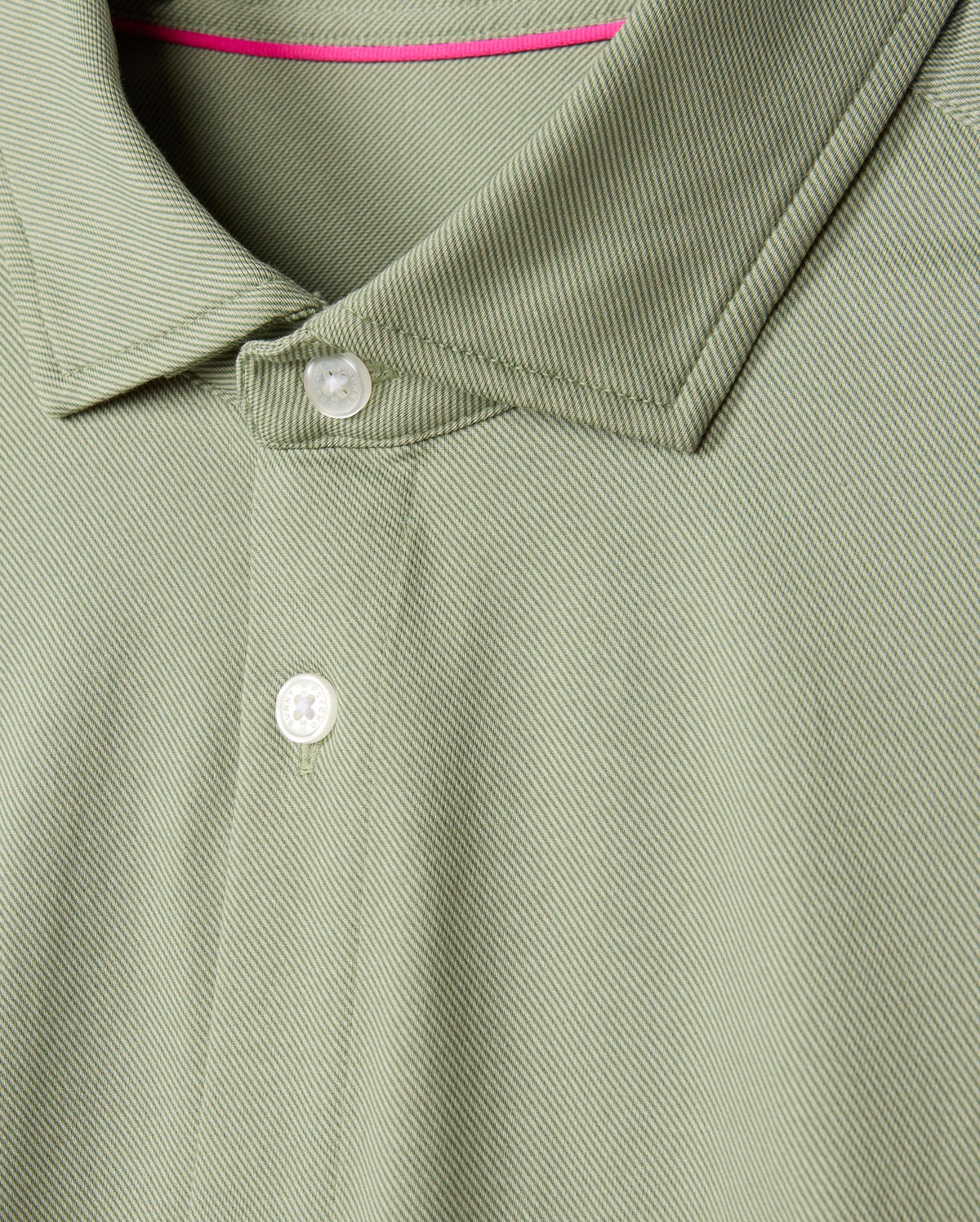 The product is a close-up of the Psycho Bunny MENS BRENDAN JERSEY SHIRT - B6C749D200, featuring a green color with white buttons, made from Pima cotton jersey. It showcases a textured pattern with a neatly folded collar and contrast piping at the inside neckline for added flair.