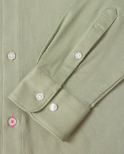 Zoom in on the sleeve of the MENS BRENDAN JERSEY SHIRT - B6C749D200 by Psycho Bunny, featuring a green, herringbone-patterned design. The sleeve showcases a cuff with three white buttons, crafted from Pima cotton jersey fabric that offers a subtle texture. A unique detail is highlighted by one buttonhole stitched with pink thread. Sophisticated contrast piping along the edges enhances its elegant appeal.