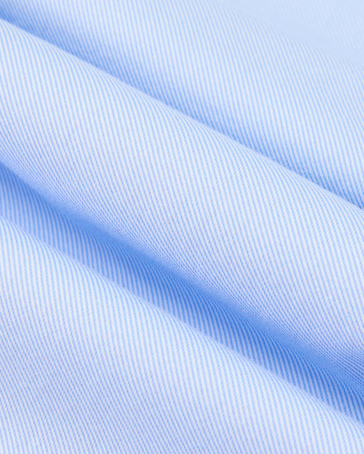 A close-up of the MENS BRENDAN JERSEY SHIRT - B6C749D200 by Psycho Bunny reveals a light blue and white striped fabric with diagonal lines that create a soft, textured appearance. Made from high-quality Pima cotton, the neatly folded shirt highlights its smooth and durable weave.