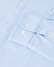 Close-up of a light blue and white pinstripe *Mens Brook Striped Jersey Shirt - B6C750D200* by Psycho Bunny, featuring white buttons on the cuff. The texture of the Pima cotton fabric is clearly visible, with an embroidered logo located near the shoulder. This comfortable shirt is neatly pressed and clean.