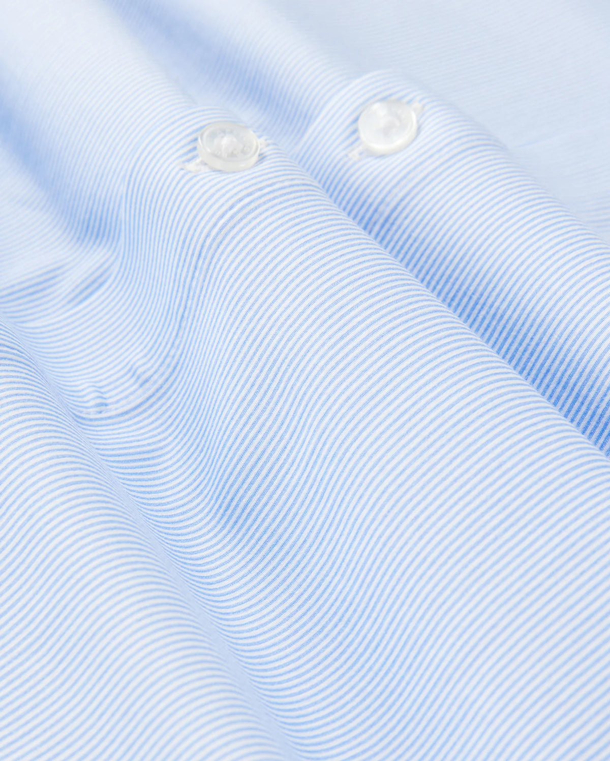 Close-up of a light blue and white striped fabric from Psycho Bunny's Men's Brook Striped Jersey Shirt, crafted from soft Pima cotton. The smooth texture and horizontal stripes create a wave-like pattern, accented by two pristine white buttons. This comfortable shirt offers both style and coziness in every detail. (Product Code: B6C750D200)