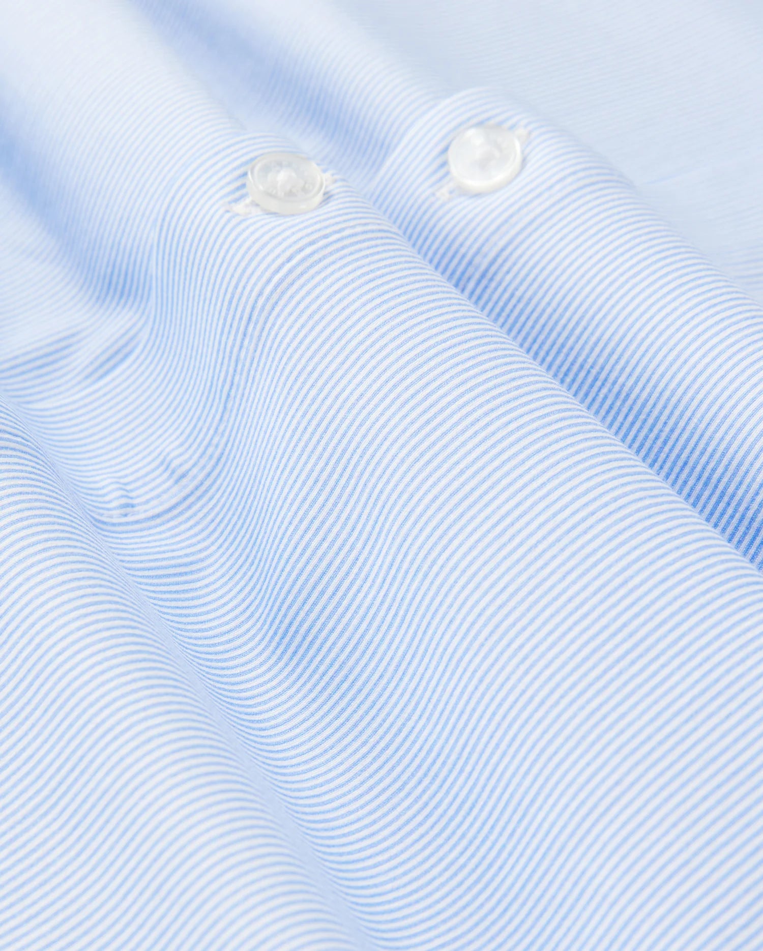 Close-up of a light blue and white striped fabric from Psycho Bunny's Men's Brook Striped Jersey Shirt, crafted from soft Pima cotton. The smooth texture and horizontal stripes create a wave-like pattern, accented by two pristine white buttons. This comfortable shirt offers both style and coziness in every detail. (Product Code: B6C750D200)