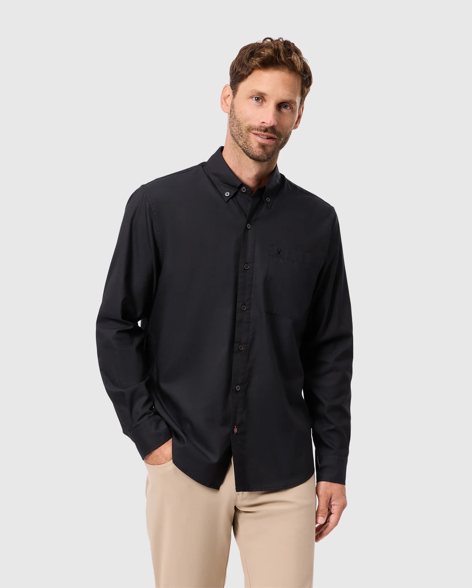 A man in a Psycho Bunny MENS JARED COTTON MODAL SHIRT and beige pants poses against a light gray background, his right hand in his pocket.