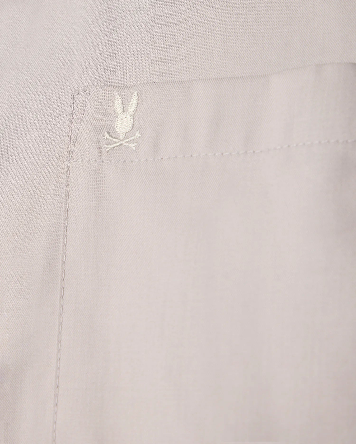 Close-up of a beige pocket on the Psycho Bunny MENS JARED COTTON MODAL SHIRT - B6C774D200, highlighting intricate stitching and an embroidered rabbit head with crossed bones.