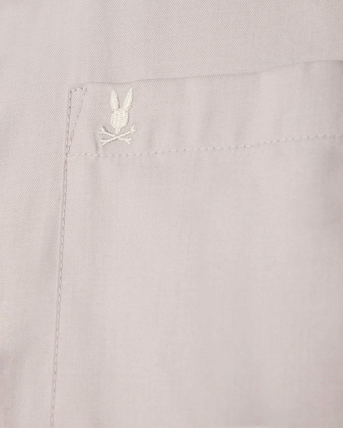 Close-up of a beige pocket on the Psycho Bunny MENS JARED COTTON MODAL SHIRT - B6C774D200, highlighting intricate stitching and an embroidered rabbit head with crossed bones.
