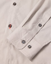 Close-up of the MENS JARED COTTON MODAL SHIRT by Psycho Bunny, showing its beige cuff with grey buttons and folded sleeve. Red thread on one buttonhole adds contrast, highlighting the detailed stitching of this premium shirt.