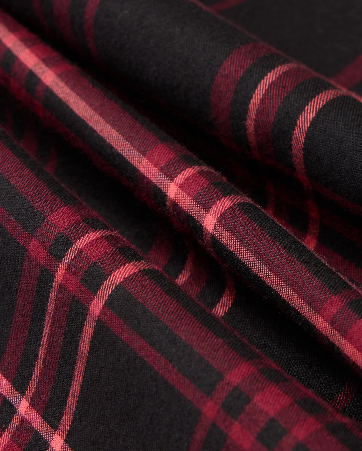 Close-up of a folded MENS HAYES PLAID SHIRT - B6C842D200 by Psycho Bunny, featuring a red and black checkered pattern crafted from luxurious Pima cotton. The intersecting horizontal and vertical lines showcase the classic design typical of a quality button-down shirt.
