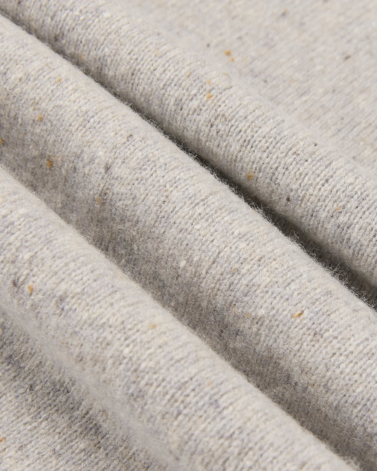 A close-up of the MENS LINCOLN MERINO WOOL SWEATER - B6E831D200 by Psycho Bunny highlights its textured merino wool fabric in light gray, adorned with subtle speckles of brown and beige. This soft, slightly ribbed surface creates gentle folds and shadows, showcasing a timeless style.