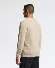 A person with short dark hair is standing and facing away, wearing a MENS LINCOLN MERINO WOOL SWEATER by Psycho Bunny in light beige, paired with dark pants against a plain white background.