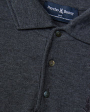 A close-up of the dark gray Men's Bradshaw Polo Sweater (B6E835D200) showcases its merino wool fabric, complete with buttons and a collar. The Psycho Bunny brand label is prominently displayed at the neck, featuring the iconic bunny logo that accentuates its luxurious appeal.