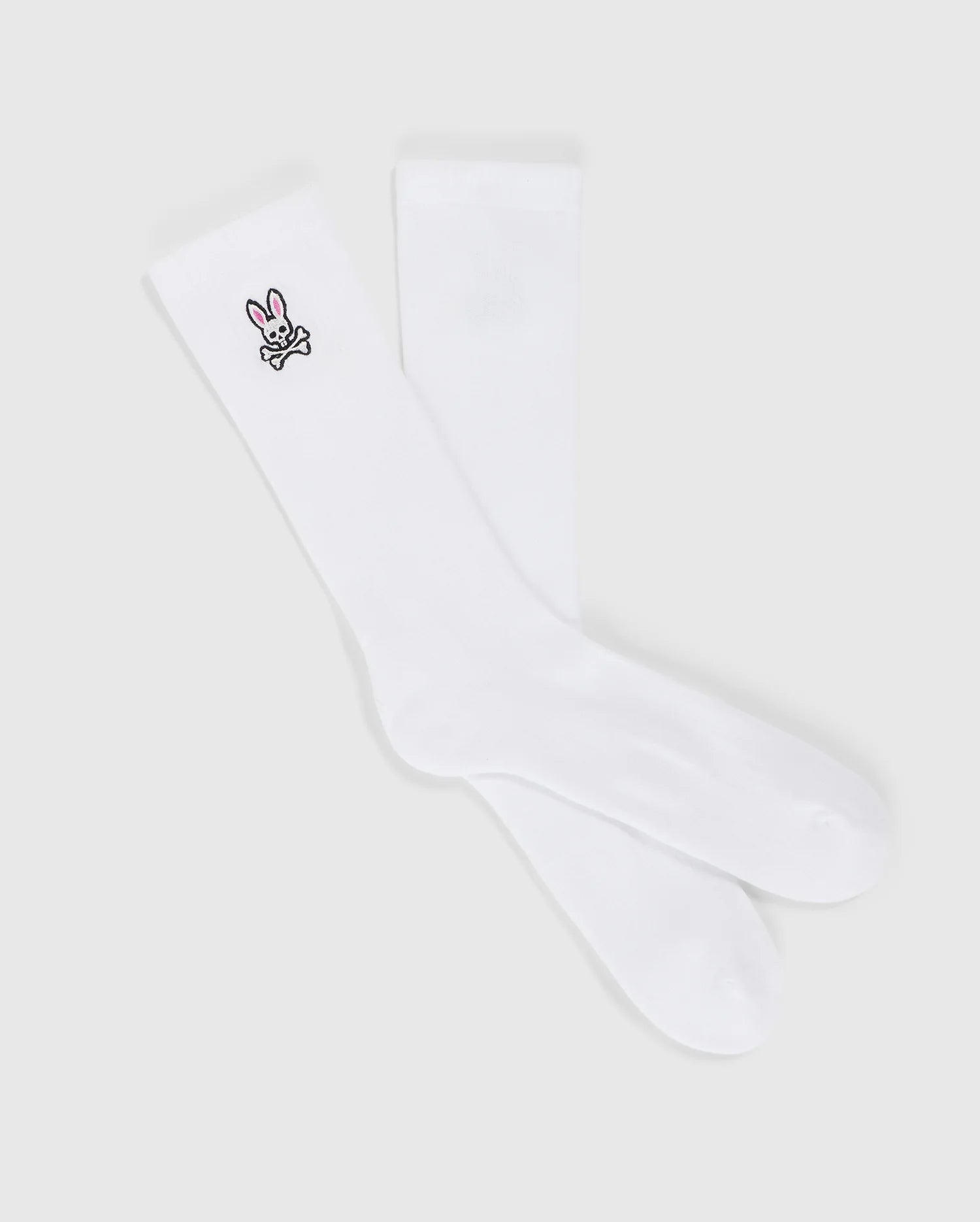 A pair of MENS FASHION SOCKS - B6F486C200 from Psycho Bunny, made from luxurious Pima cotton, featuring a small embroidered bunny design near the top. The bunny is depicted in black outline with a pink nose and ears, adorning only one sock. These stylish socks are made in Peru and offer both comfort and charm.