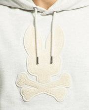 The Psycho Bunny MENS ELDORADO BRUSH BACK HOODIE (B6H234E200) features a gray applique of a stylized bunny head with long ears over crossed bones, reminiscent of a pirate flag. Its brush-back design offers comfort and a textured monochrome look, perfect for swaddle season.