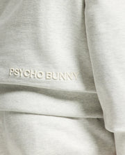Close-up of the Psycho Bunny Mens Eldorado Brush Back Hoodie, featuring "PSYCHO BUNNY" embroidered in white on light gray, ideal for swaddle season with its cozy brush-back fabric.