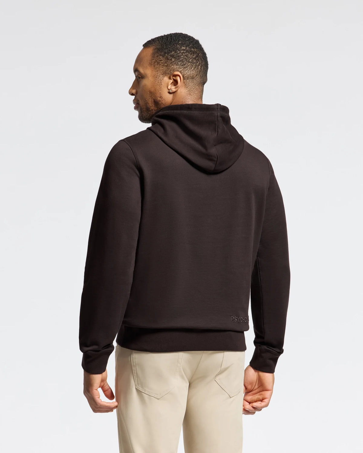 A person wearing a Psycho Bunny MENS ELDORADO BRUSH BACK HOODIE - B6H234E200 in black and beige pants stands with their back to the camera against a plain white background.