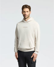A man with medium-length brown hair and a beard wears the light beige Psycho Bunny Mens Nora Classic French Terry Hoodie (B6H434F200) featuring an "Apres Sunday" embroidered logo on the chest. He stands against a plain white background, hands relaxed by his sides.