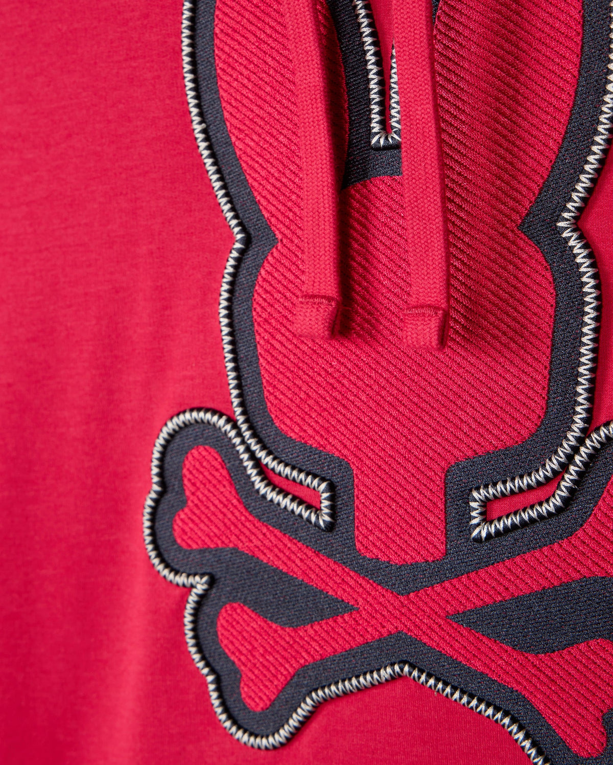 Zoomed-in view of the red MENS WALTER LIGHTWEIGHT HOODIE - B6H476D200 by Psycho Bunny, crafted from Micro French Terry. It displays a stitched design of a stylized rabbit with crossed bones beneath it, using black and white thread. The texture of the fabric and the intricate 3D outlined embroidery stand out clearly.