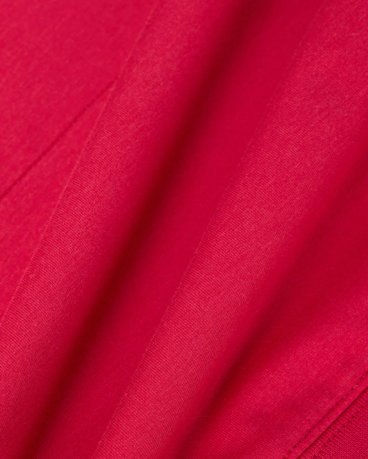 A close-up of the vibrant red fabric from the Psycho Bunny MENS WALTER LIGHTWEIGHT HOODIE - B6H476D200 highlights its smooth texture and gentle folds, evoking an elegance reminiscent of delicate craftsmanship.