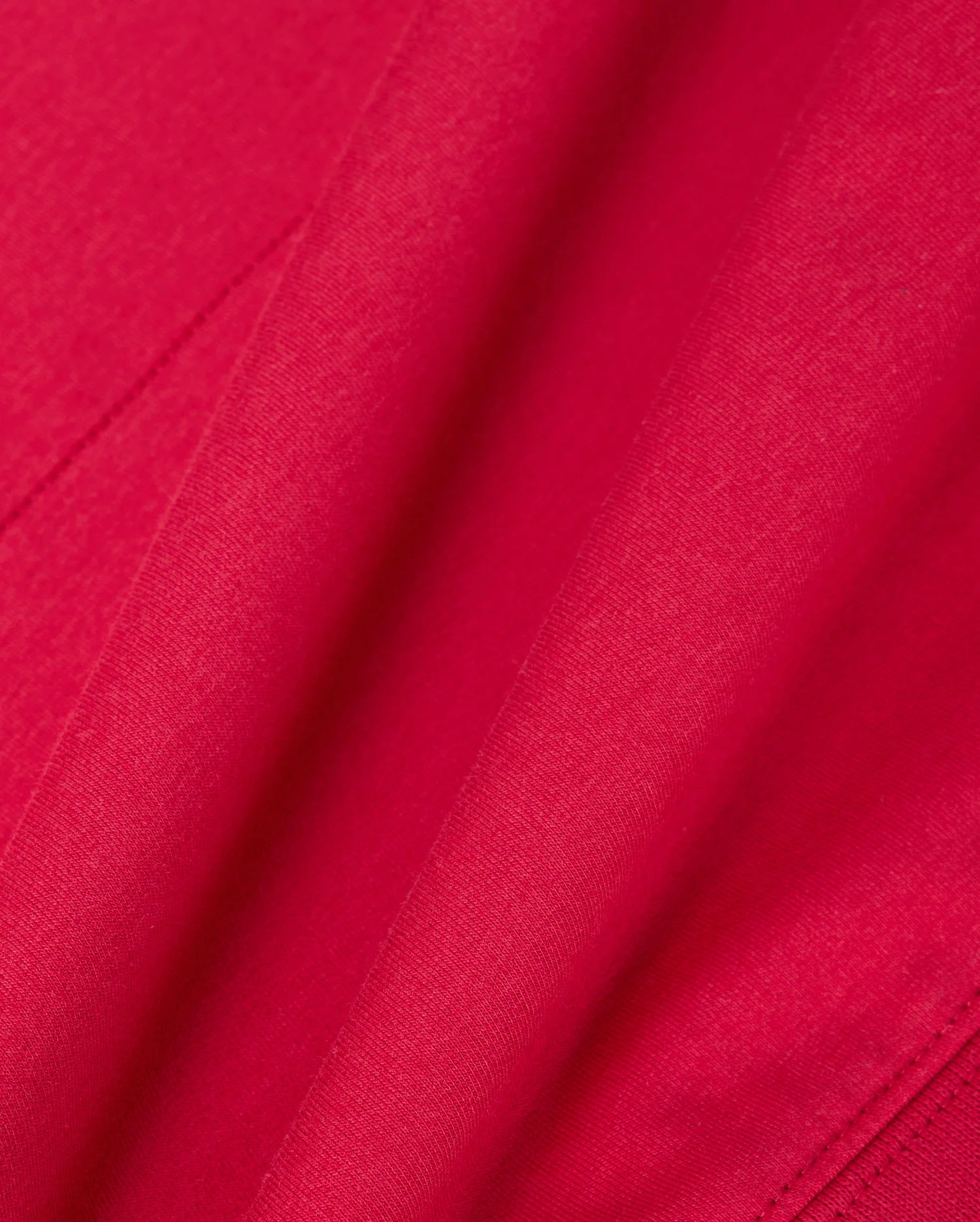 A close-up of the vibrant red fabric from the Psycho Bunny MENS WALTER LIGHTWEIGHT HOODIE - B6H476D200 highlights its smooth texture and gentle folds, evoking an elegance reminiscent of delicate craftsmanship.