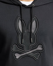 A close-up of Psycho Bunny's MENS NEW CASTLE FRENCH TERRY HOODIE (B6H517F200): an elegant black hoodie with a soft French terry fabric, showcasing a stylized embroidered bunny head and crossbones motif in gray shades on the front.