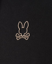 Close-up of the Psycho Bunny MENS JAMES PREMIUM HOODIE - B6H789D200, showcasing an embroidered design in white thread on its premium jersey fabric. The design features a silhouette of rabbit ears above crossbones, delivering a playful and slightly edgy visual. The embroidery is centered in the image.