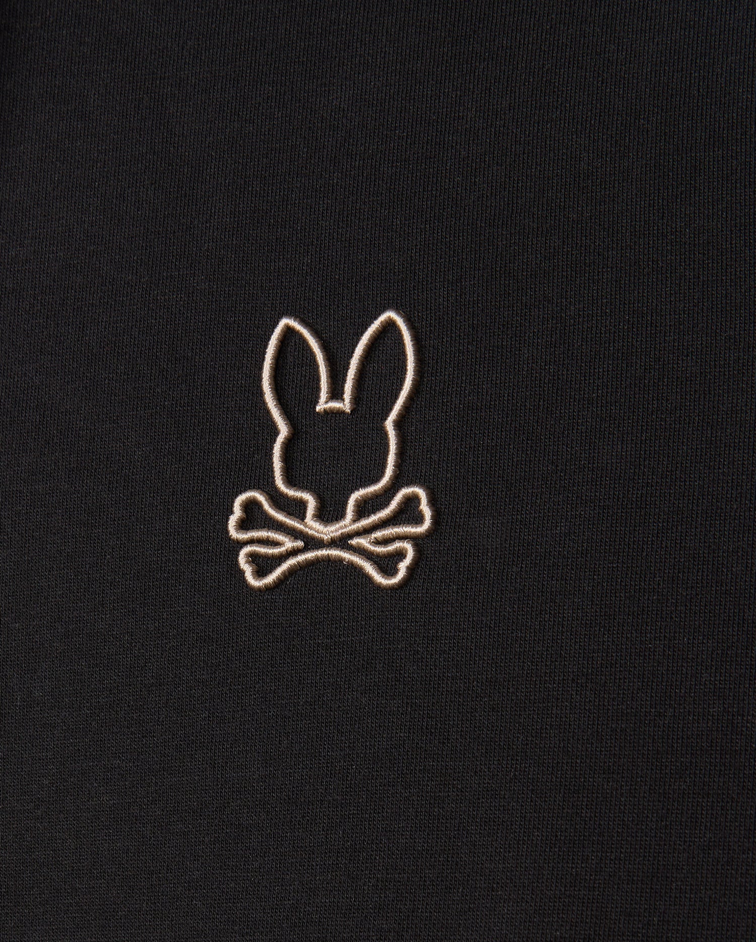 Close-up of the Psycho Bunny MENS JAMES PREMIUM HOODIE - B6H789D200, showcasing an embroidered design in white thread on its premium jersey fabric. The design features a silhouette of rabbit ears above crossbones, delivering a playful and slightly edgy visual. The embroidery is centered in the image.