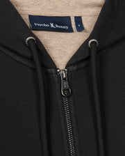 Close-up of a black MENS JAMES PREMIUM ZIP HOODIE - B6H793D200 featuring a zipper and drawstrings. The interior of the hood is a contrasting beige color. A clothing label above the zipper reads "Psycho Bunny," with an embroidered Bunny graphic next to it, crafted from double-faced premium jersey material.