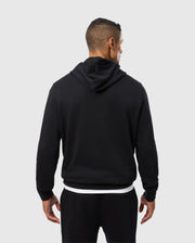 A person stands facing away, dressed in Psycho Bunny's Men's Pacific Chenille Hoodie in black, paired with matching black pants. Against a plain, light gray background, the emphasis is on the hoodie's design and fit, highlighted by its soft cotton knit fabric.