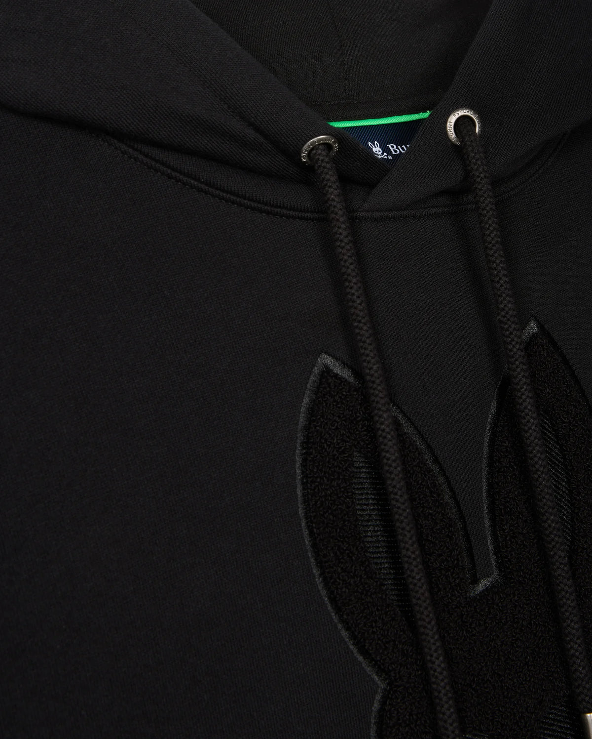 Close-up of a black Psycho Bunny Men's Pacific Chenille Hoodie, model B6H930D200, boasting drawstrings and an adorable furry rabbit ear design. A small hint of the blue tag is visible inside the neckline, adding charm to this cozy piece.