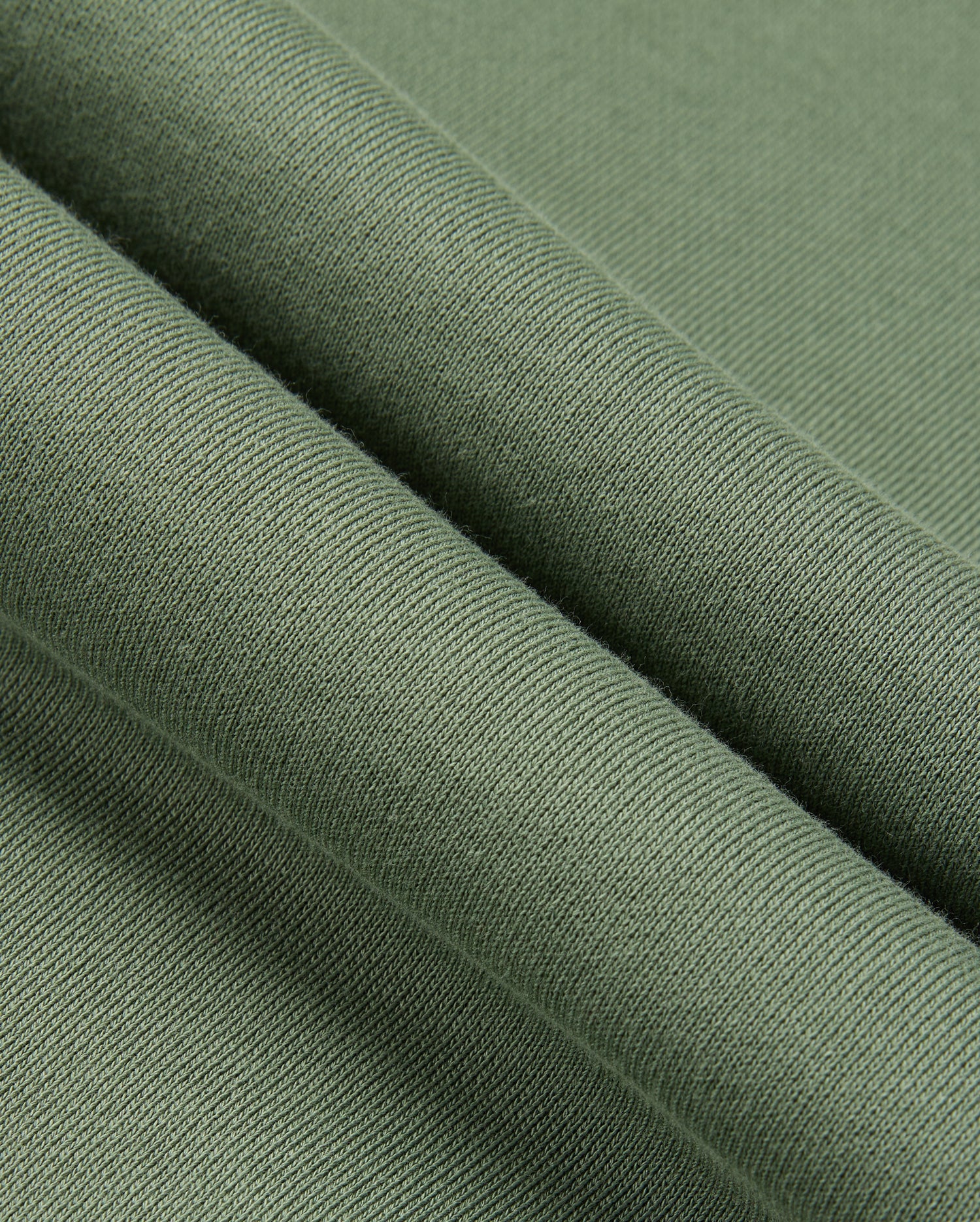 A close-up of the green fabric, resembling the cozy texture of a Psycho Bunny MENS PACIFIC CHENILLE HOODIE (B6H930D200), showcases its smooth feel and fine knitting. The folded fabric highlights its softness and uniform weave, much like luxurious chenille embroidery.