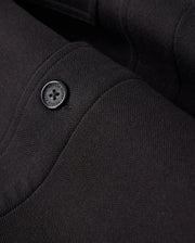 Zoomed-in view of the black fabric from the MENS BEDFORD SHIRT JACKET - B6J290B200 by Psycho Bunny, highlighting the texture and stitching details with a single black button, reminiscent of a work-jacket style.