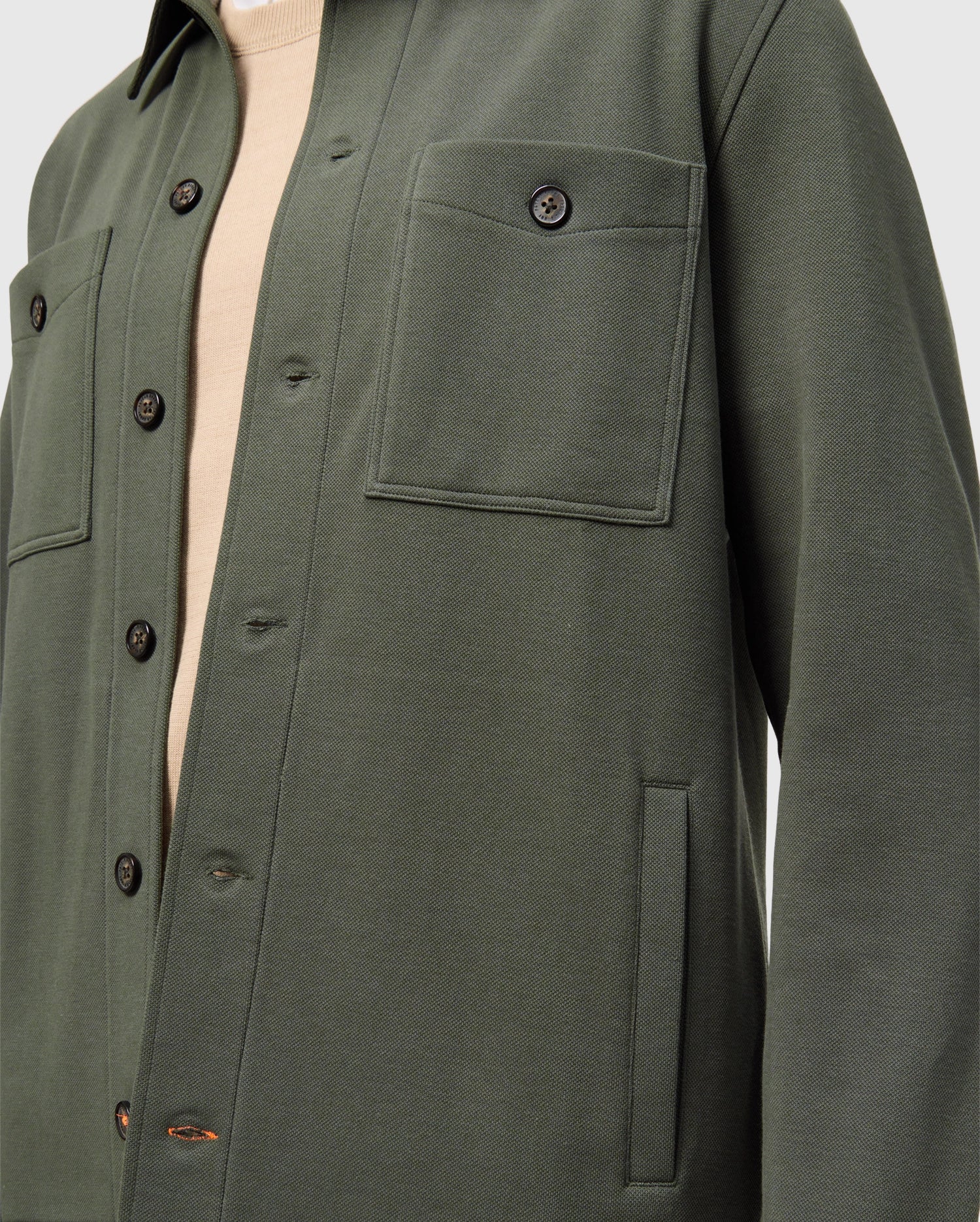 Close-up of a person wearing the Psycho Bunny MENS BEDFORD SHIRT JACKET - B6J290B200 in dark green over a beige shirt. This cotton-blend overshirt, with its urban vibe, showcases two chest pockets and black buttons.