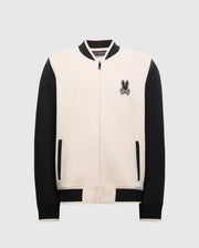 Introducing the Psycho Bunny MENS CRETE COLOR BLOCK BOMBER - B6J421F200: a varsity-style jacket with cream front, black sleeves, and trim. Featuring a rabbit crossbones logo on the chest, it's perfect for transitions with its zipper and side pockets.