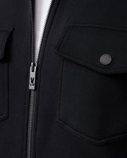 Close-up of the MENS OROVILLE BOMBER JACKET - B6J712A200 by Psycho Bunny, a black bomber jacket featuring a zipper with the brand's distinctive bunny logo on the pull. This outerwear piece showcases two snap-button flap pockets, crafted from a smooth and slightly textured cotton-poly fabric blend.