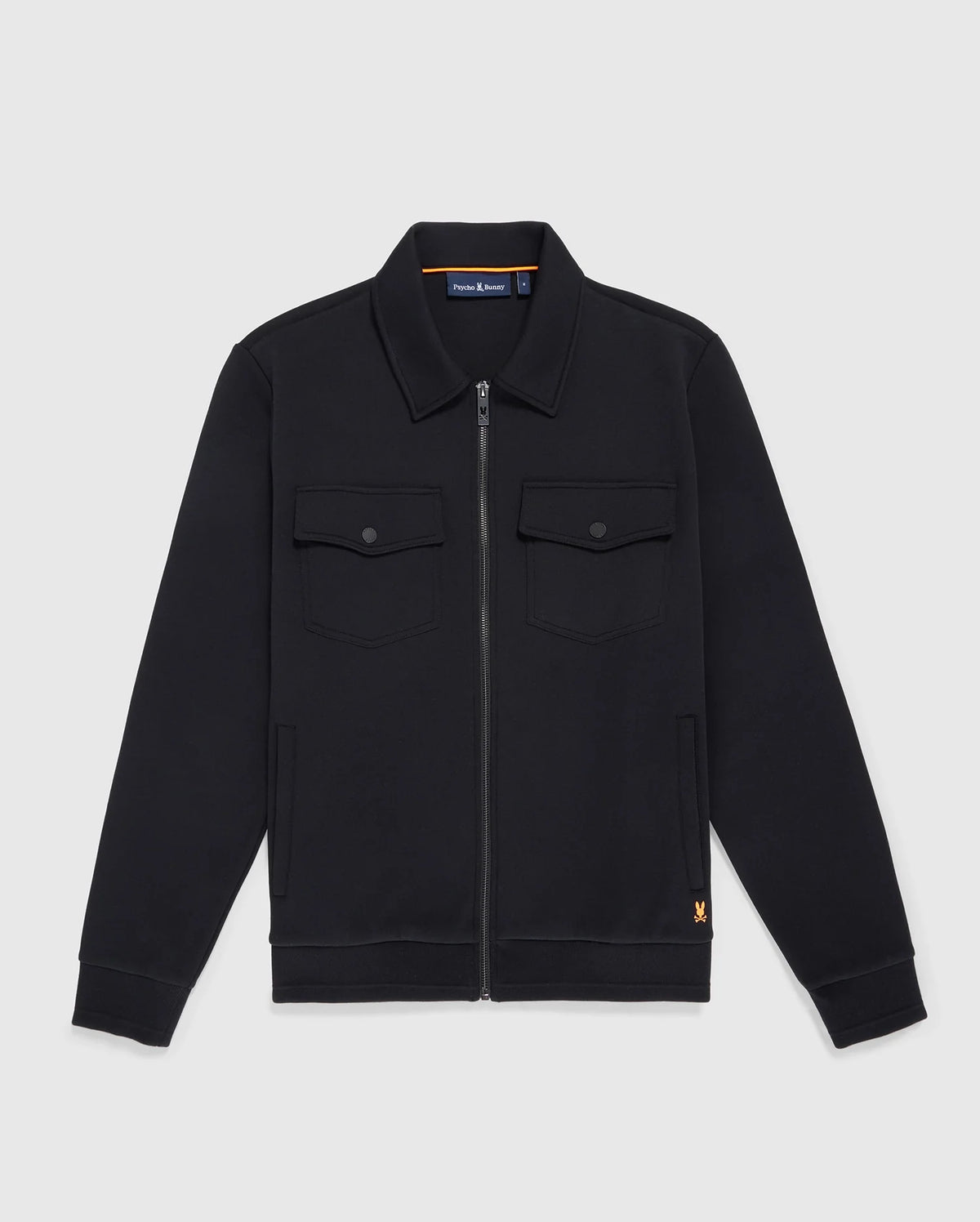 The MENS OROVILLE BOMBER JACKET - B6J712A200 from Psycho Bunny is a black zip-up cotton-poly jacket with a collar and long sleeves. This outerwear includes two buttoned chest pockets and showcases a small orange logo near the hem, set against a plain white background.