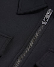 Close-up of the Psycho Bunny MENS OROVILLE BOMBER JACKET - B6J712A200 in black, showcasing a silver zipper with an engraved logo. The smooth cotton-poly fabric and the design featuring folded-over edges hint at a pocket or flap detail near the zipper, enhancing its sleek outerwear appeal.