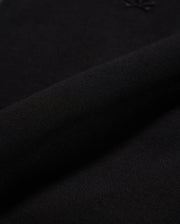Close-up of the MENS OROVILLE BOMBER JACKET - B6J712A200 by Psycho Bunny, made from black cotton-poly fabric. The fabric is smooth and tightly woven with a subtle shine, perfect for outerwear. It appears soft and flexible, with a small embossed logo visible in the top right corner, making it ideal for crafting stylish bomber jackets that offer both elegance and comfort.