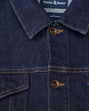 Close-up of the MENS PATHE DENIM JACKET - B6J741X1CO, showcasing its collar and two-button design. The label at the neck reads "Psycho Bunny." Visible stitching adds detail to the rugged fabric, making it a standout piece in men's fashion.