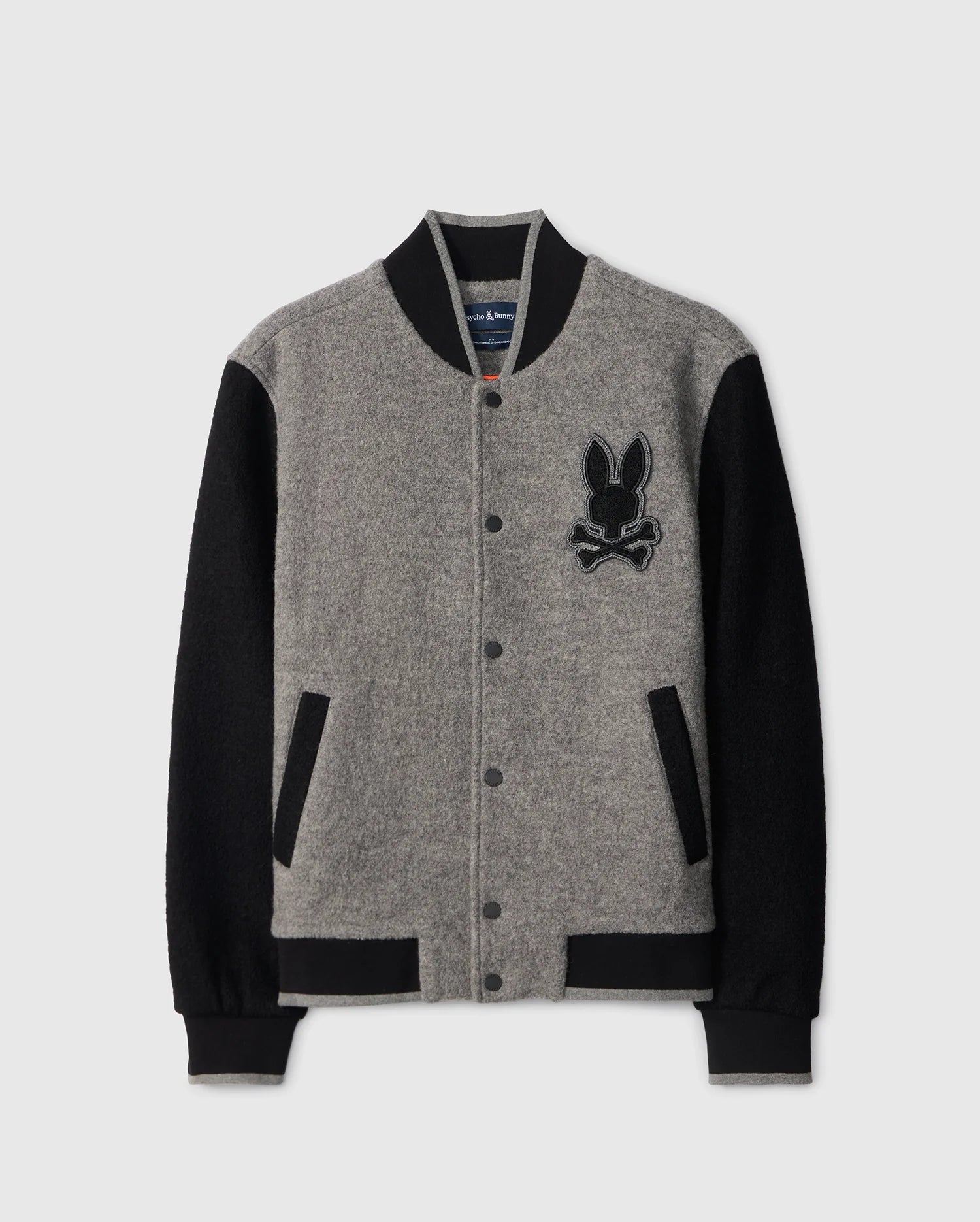 Introducing the Psycho Bunny MENS TOM WOOL BOMBER JACKET - B6J744D200, a sophisticated gray and black bomber crafted from luxurious wool. Featuring a distinctive rabbit and crossbones logo on the chest, this jacket offers black sleeves, a contrasting black collar, and a button-up front with practical pockets—ideal for the fashion-forward gentleman.