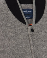 Close-up of the MENS TOM WOOL BOMBER JACKET - B6J744D200 by Psycho Bunny in grey, featuring a black collar and black buttons. The elegant touch is enhanced by a blue label with the Psycho Bunny logo visible on the inside.