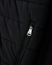 Close-up of the MENS MYKEL MIXED MEDIA JACKET by Psycho Bunny, showcasing a black quilted design with a silver zipper featuring an engraved logo. The versatile jacket includes horizontal line stitching for added texture.