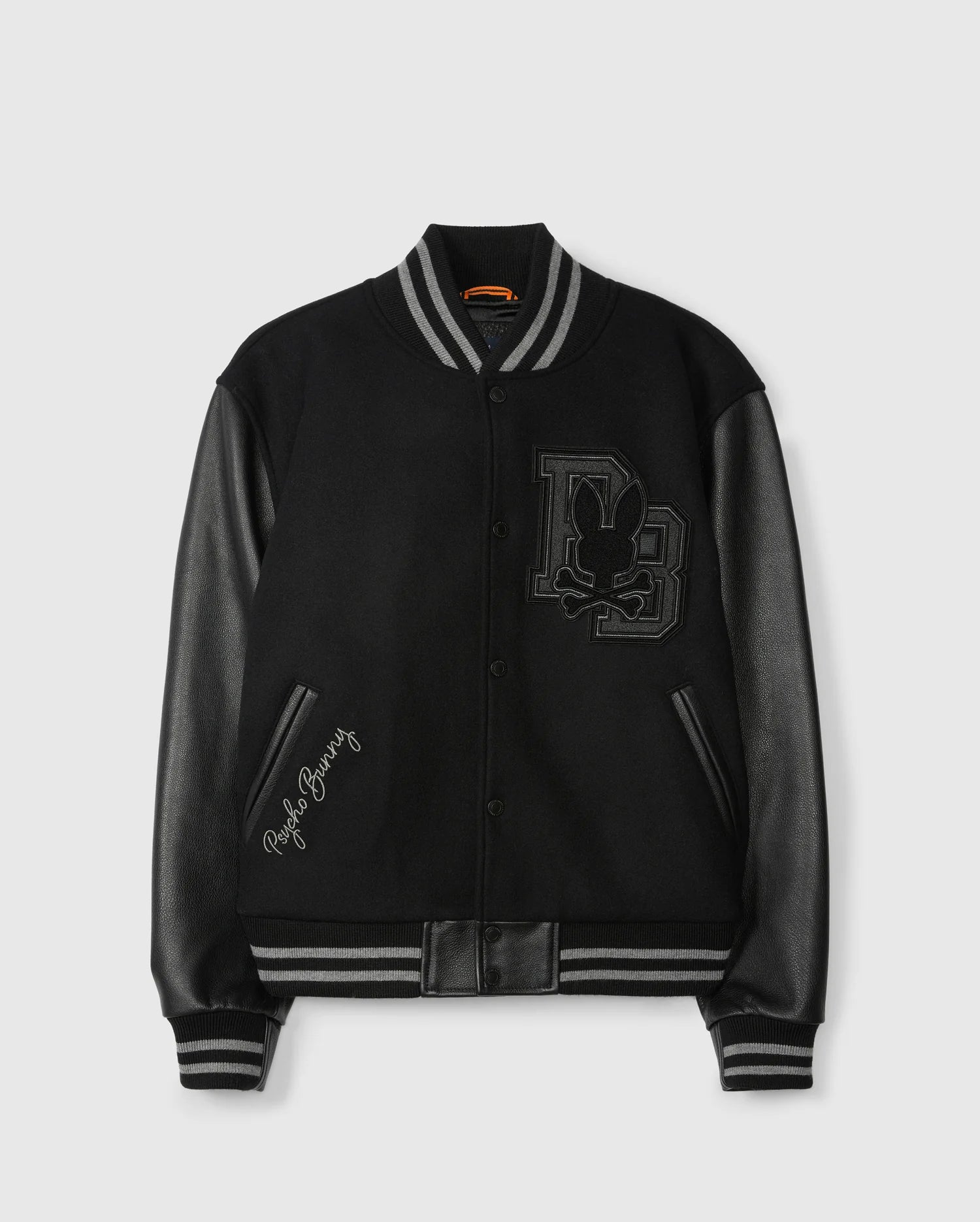 Presenting the Psycho Bunny Men's Brayden Wool Leather Varsity Bomber (B6J876D200): a sleek black jacket featuring eye-catching leather sleeves, striped cuffs, and a striking embroidered patch on the chest with initials and a rabbit silhouette. The phrase "Playboy Bunny" is elegantly stitched near the pocket for added flair.
