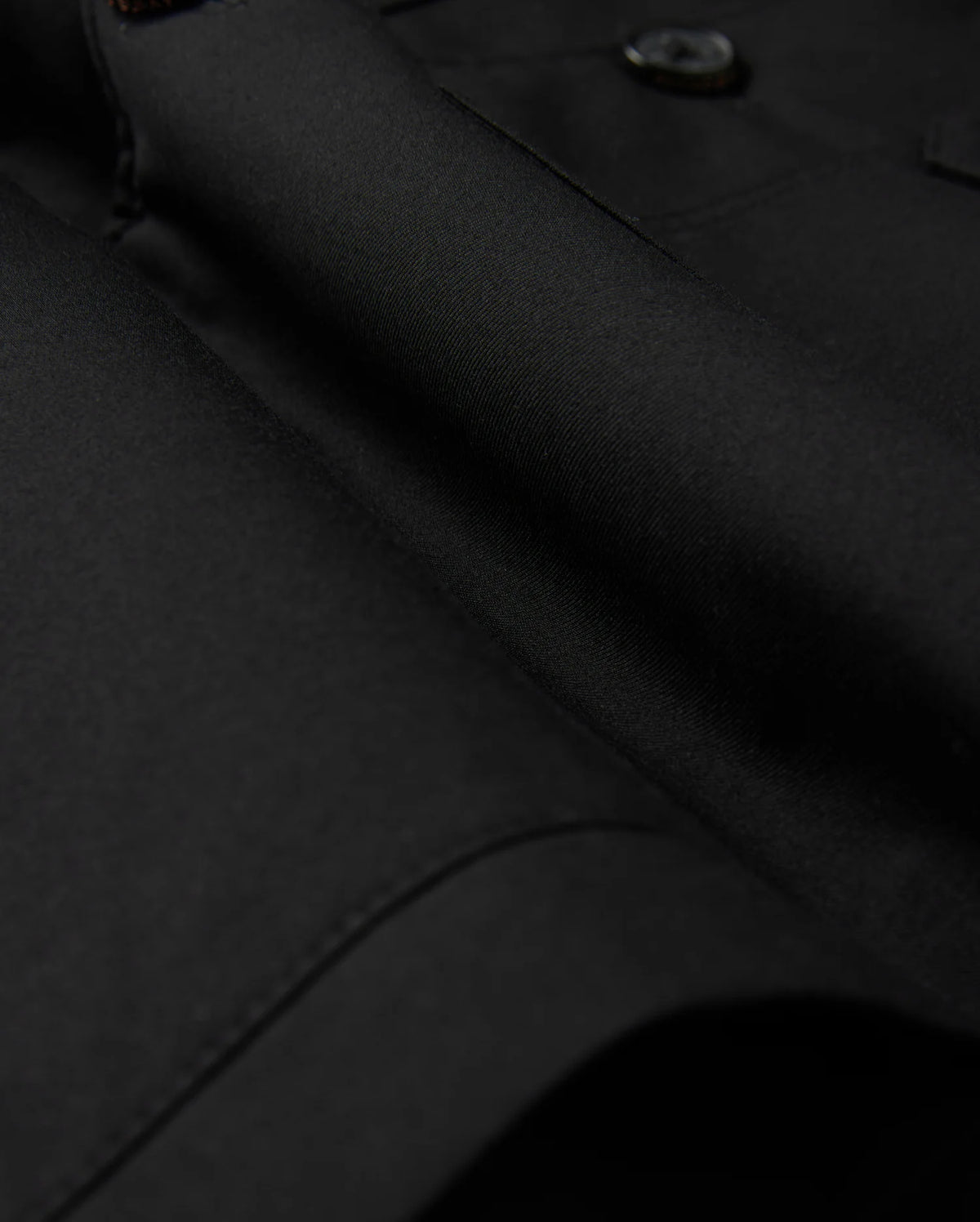 Close-up of the Psycho Bunny MENS HILLCREST PADDED SHACKET - B6J936D200, featuring sleek black fabric with button details. The dense, finely woven material has a smooth, glossy texture and subtle lighting emphasizes its luxurious finish.