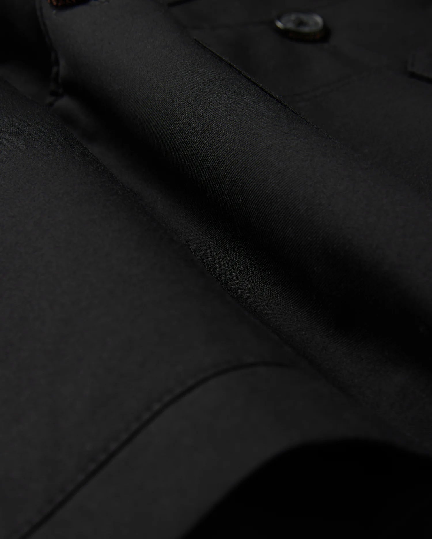 Close-up of the Psycho Bunny MENS HILLCREST PADDED SHACKET - B6J936D200, featuring sleek black fabric with button details. The dense, finely woven material has a smooth, glossy texture and subtle lighting emphasizes its luxurious finish.