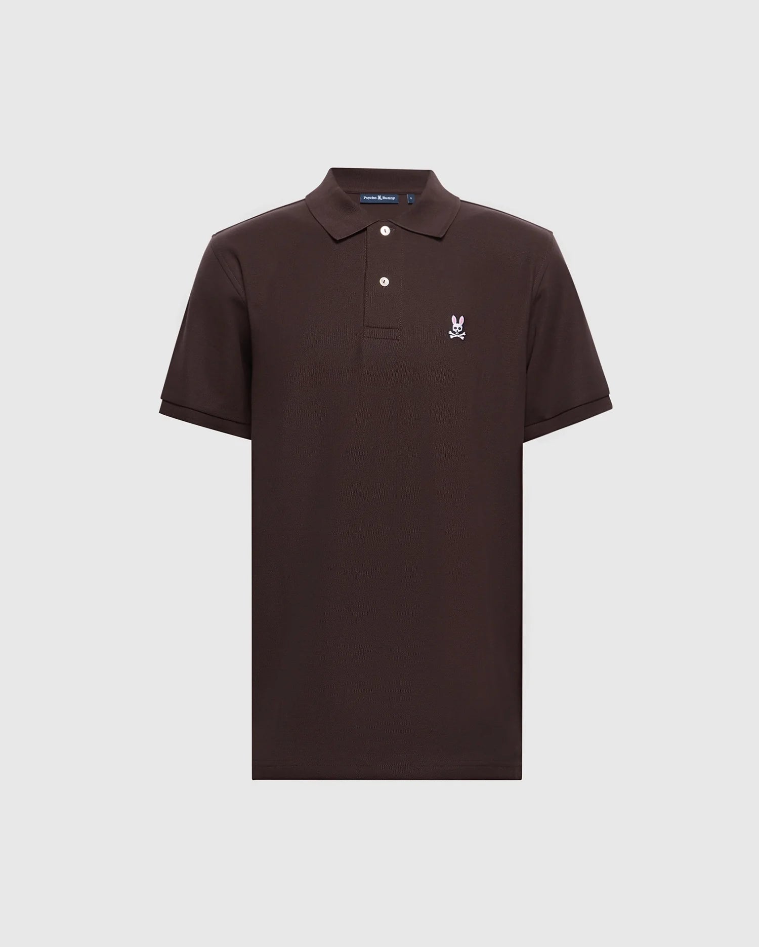 The Men's Classic Piqué Polo Shirt - B6K001D200 by Psycho Bunny is a dark brown polo crafted from soft diamond-knit piqué fabric. It has short sleeves, a collar, and a two-button placket, featuring an embroidered white skull with bunny ears logo on the upper left chest against a light gray background.
