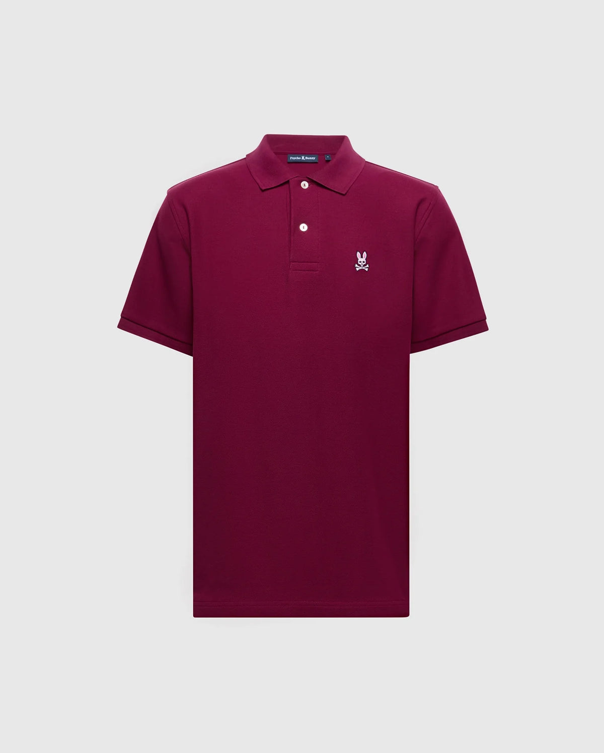 The Psycho Bunny MENS CLASSIC PIQUE POLO SHIRT - B6K001Z1PC is a burgundy short-sleeve crafted from soft Pima cotton, featuring a collar, two buttons, and a small embroidered Bunny logo on the left chest. It is displayed against a plain light gray background.
