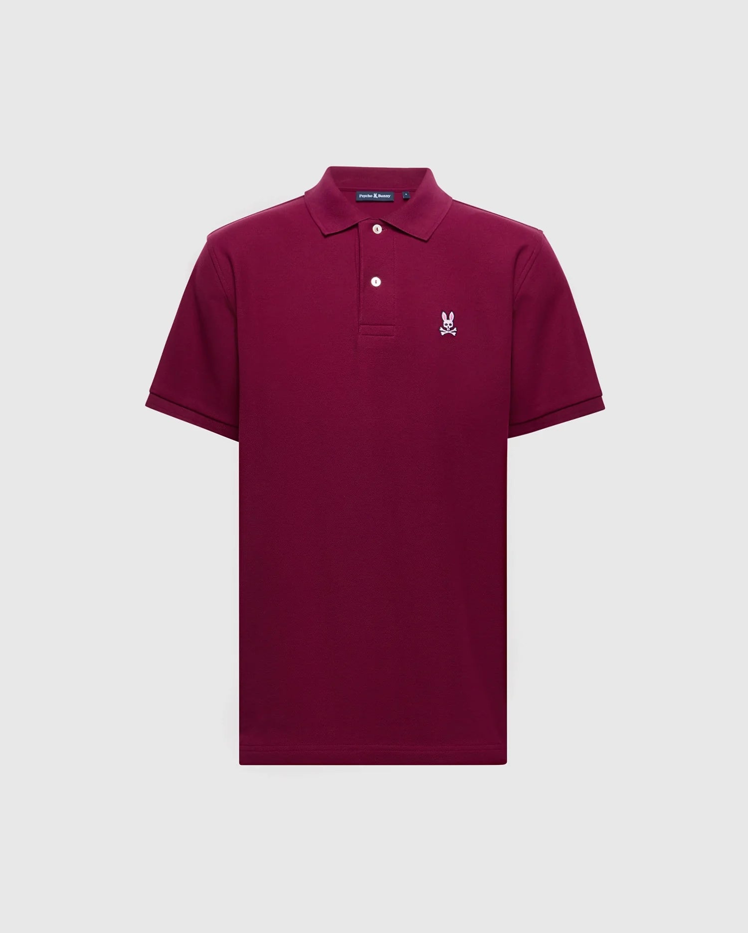 The Psycho Bunny MENS CLASSIC PIQUE POLO SHIRT - B6K001Z1PC is a burgundy short-sleeve crafted from soft Pima cotton, featuring a collar, two buttons, and a small embroidered Bunny logo on the left chest. It is displayed against a plain light gray background.