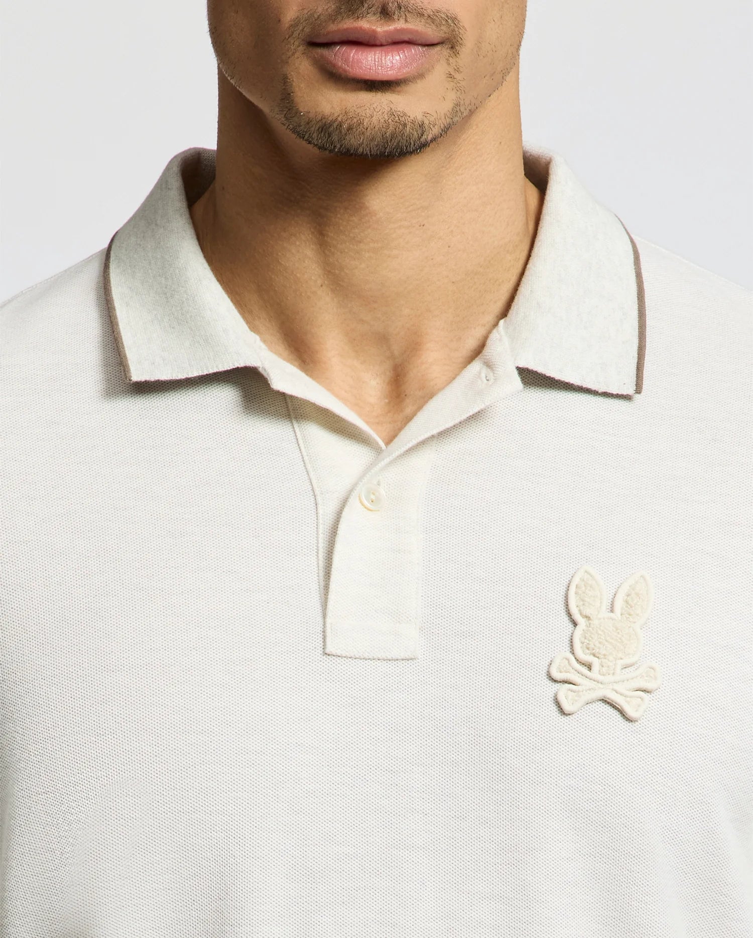 Partially visible is a person in a regular fit MENS ELDORADO PIQUE POLO by Psycho Bunny. Made from luxurious Peruvian Pima cotton, it features a collar and the iconic bunny above crossed bones patch, emphasizing its timeless appeal.
