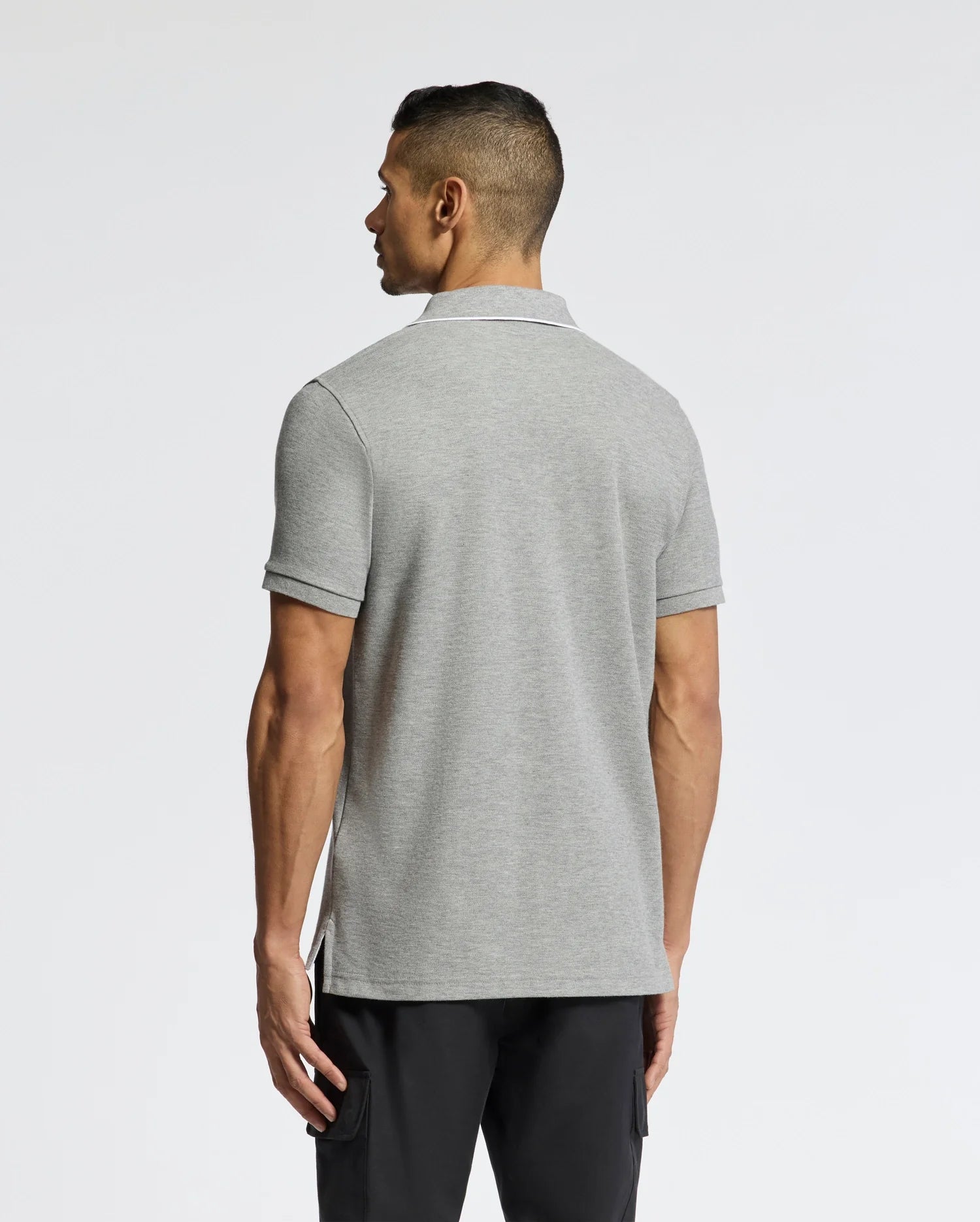 A man in a Psycho Bunny's MENS ELDORADO PIQUE POLO - B6K105E200 and black pants stands with his back to the camera against a plain backdrop.